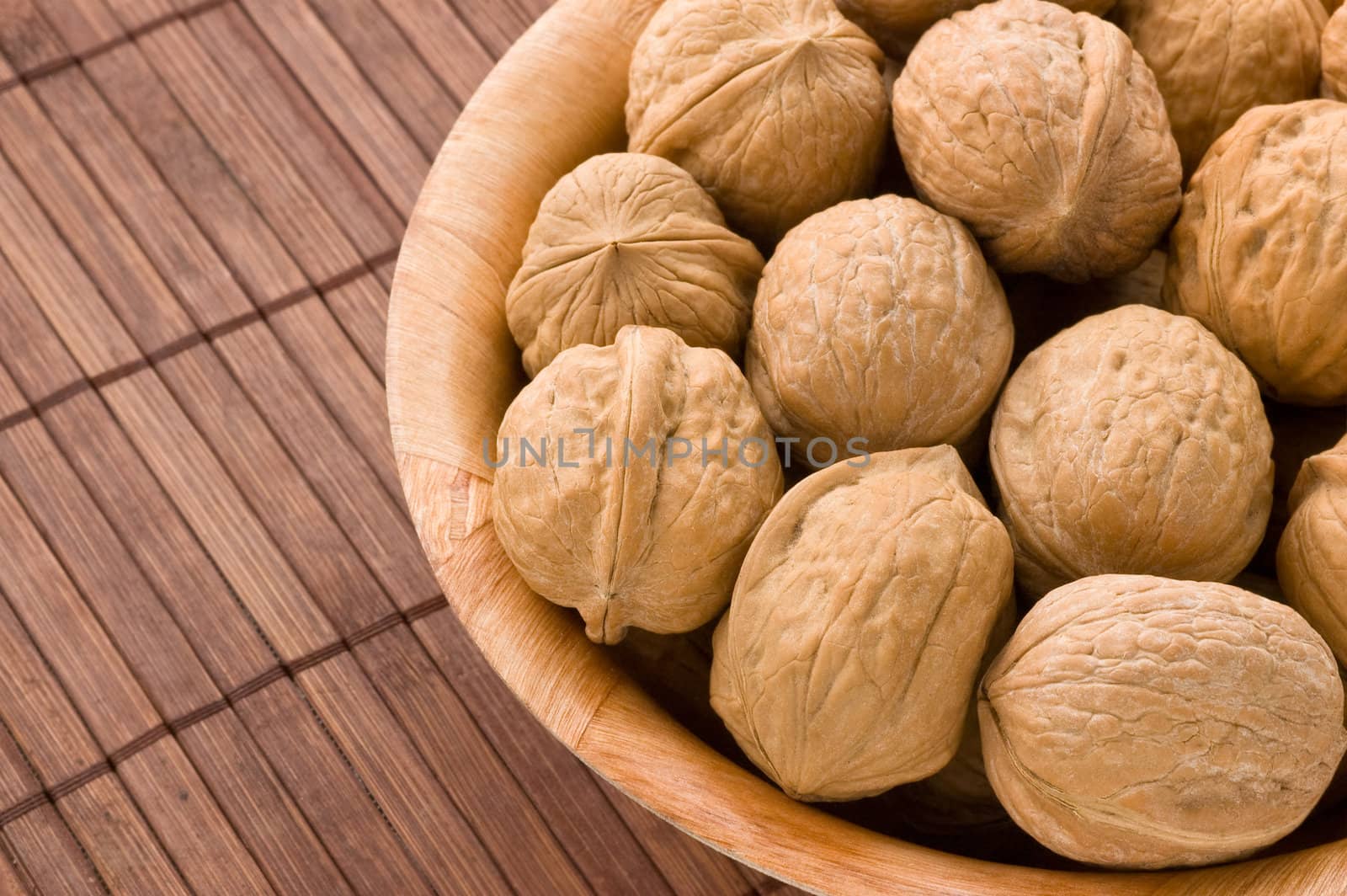 Bunch of walnuts in a bowl, over a bamboo mat.