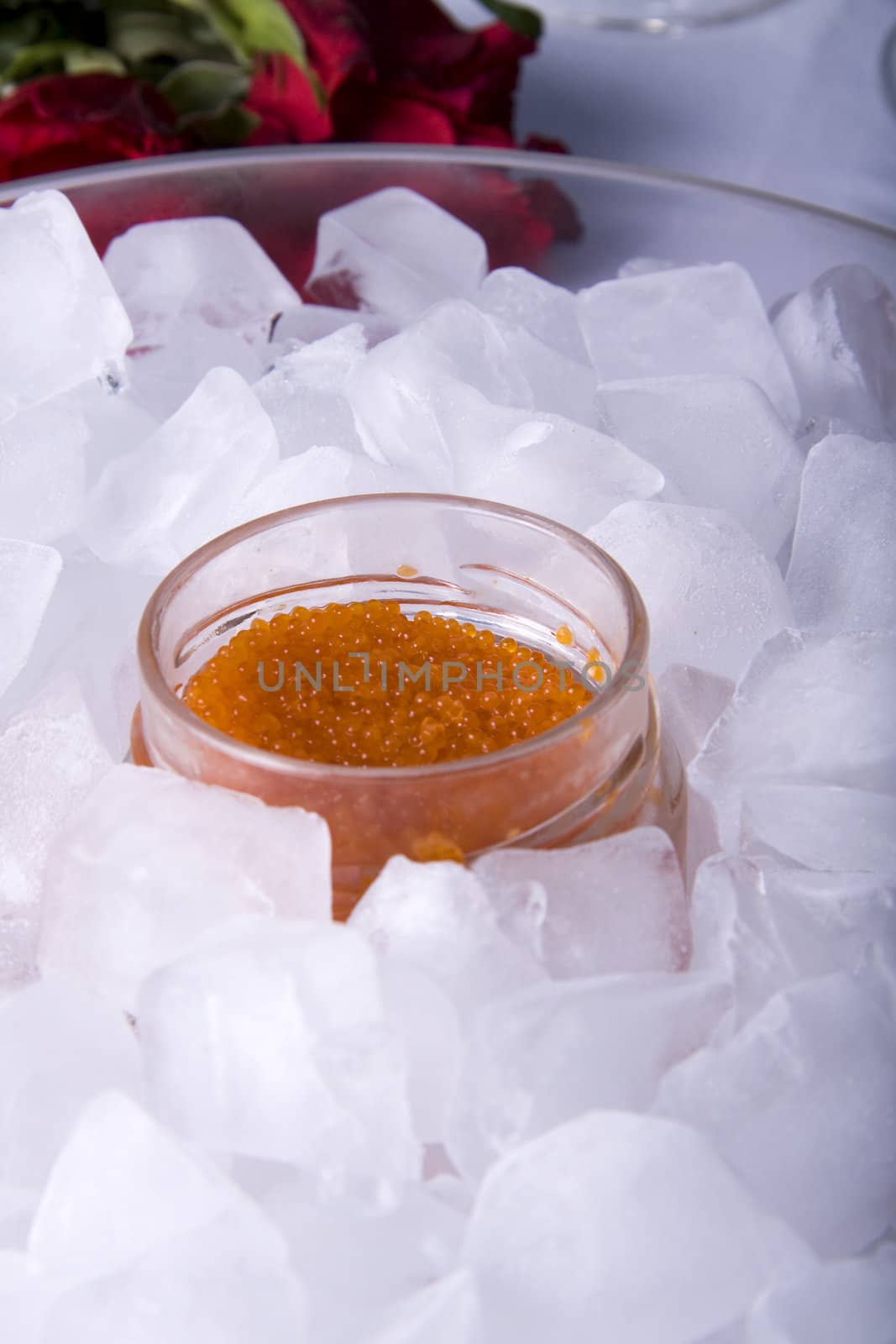 Red caviar in a glass jar surrounded by ice cubes and a rose