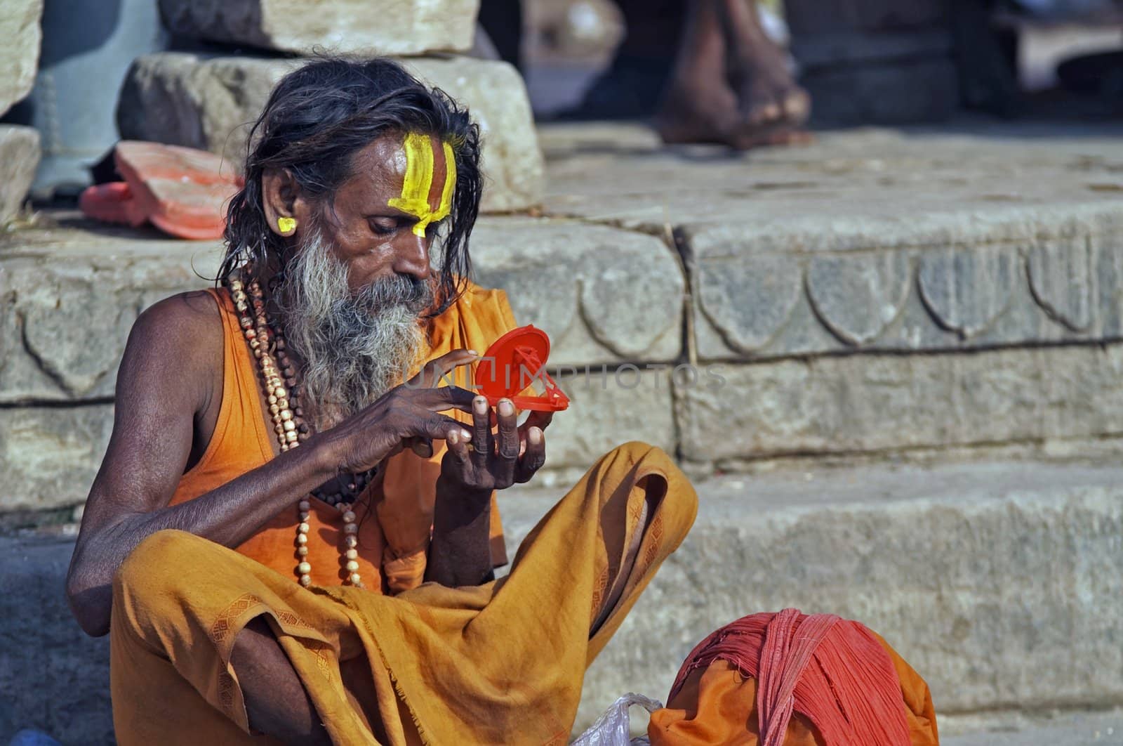 Religious man in saffron colored robes decorating his forehead with paint, Varanasi, India