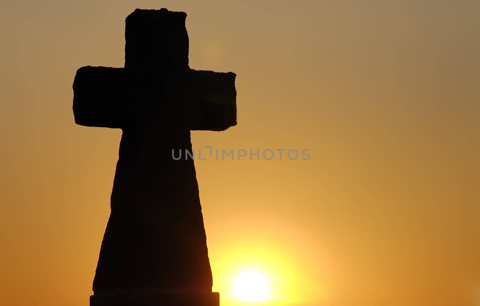a stone cross with a sunset in the background