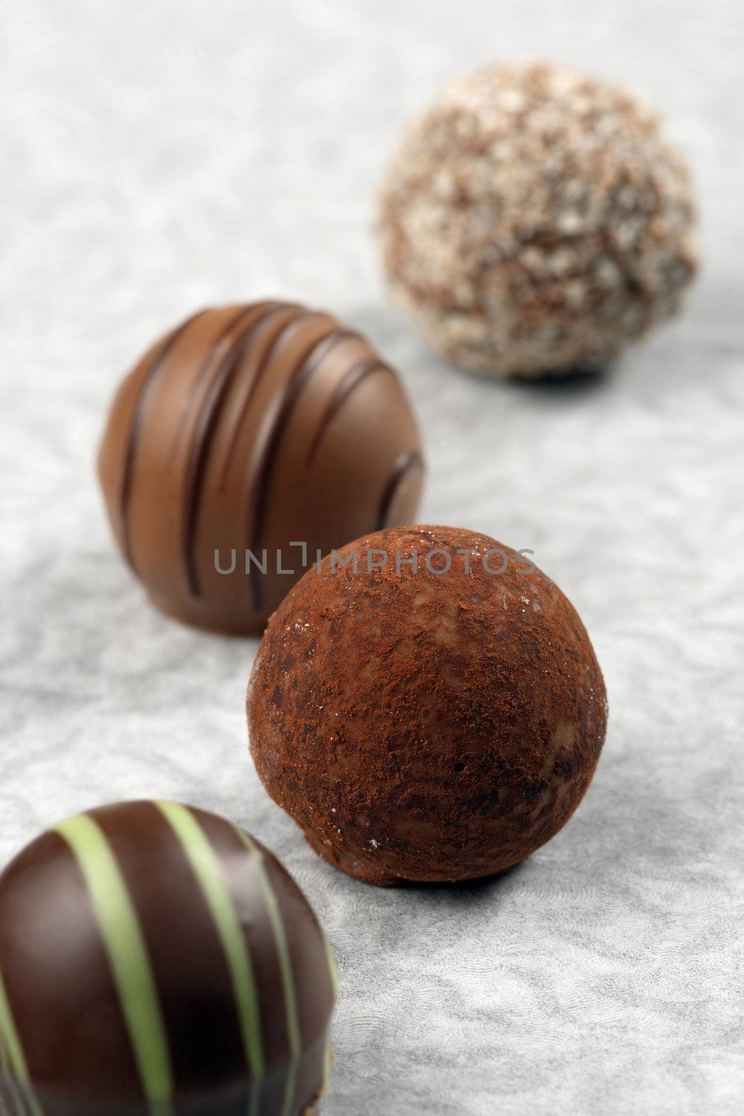 A small assortment of chocolate truffles and pralines on paper.  Very Shallow depth of field, focusing on middle truffle.
