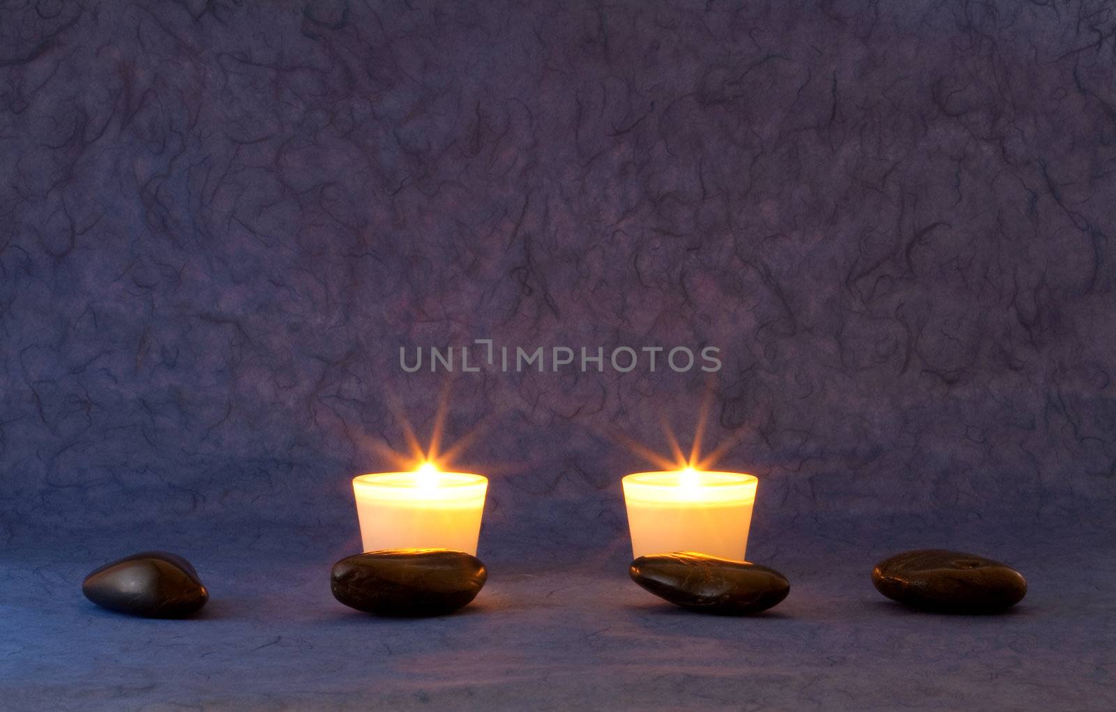A set of massage stones on blue/purple wallpaper with candles