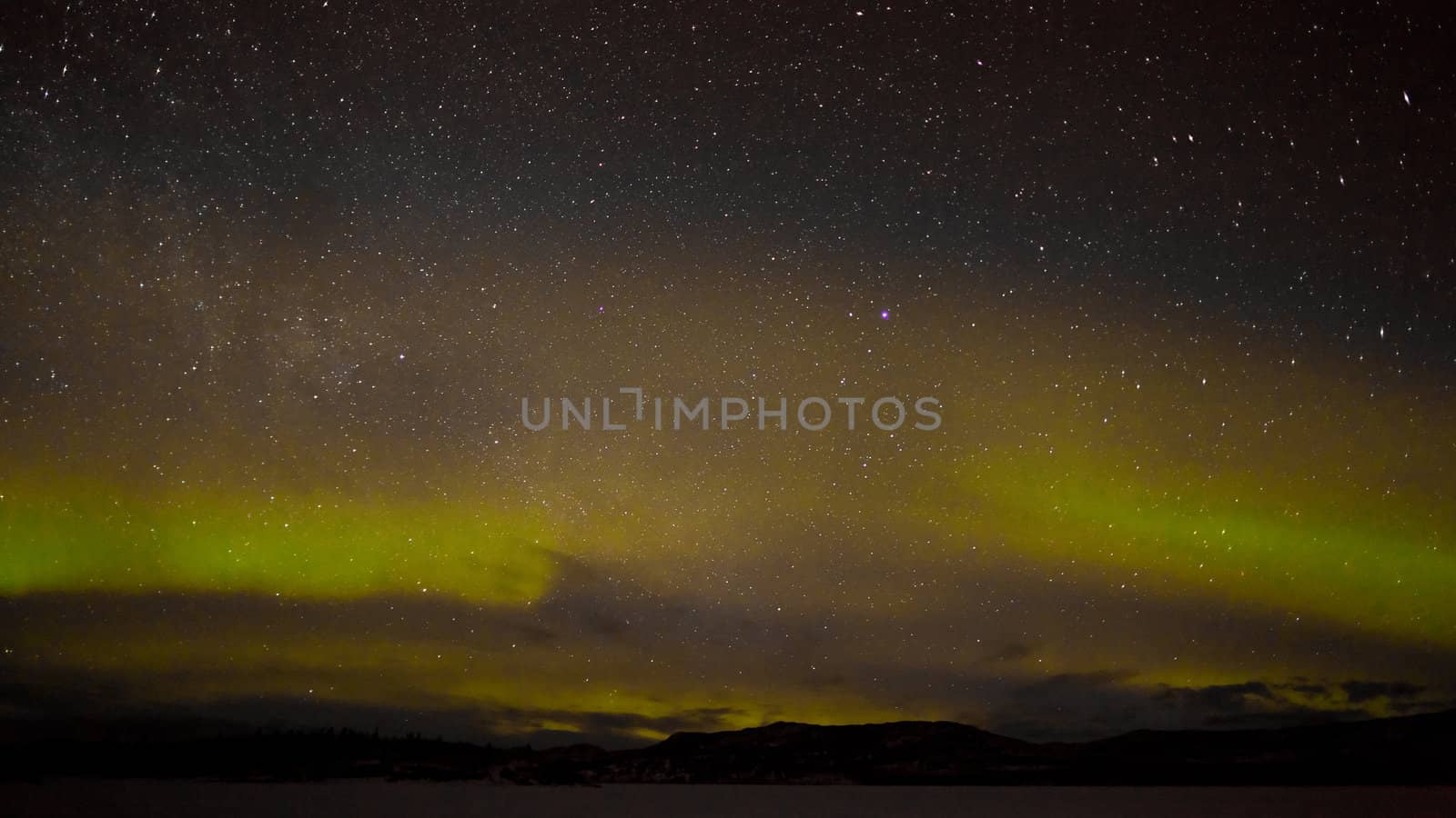 Night sky with myriad of stars with northern lights (aurora borealis) substorm above silhouette of hills and clouds.