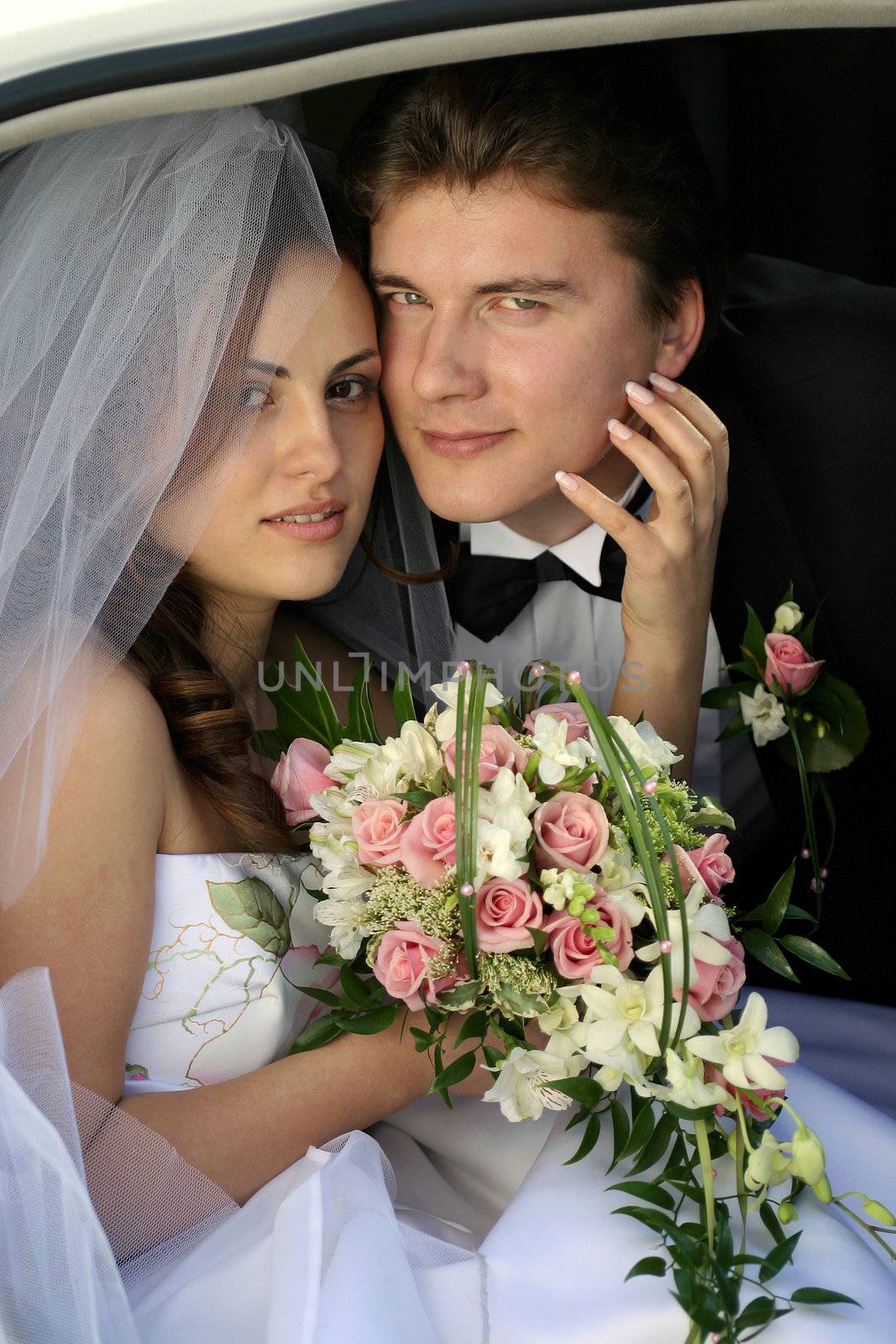 Smiling newlywed young girl in wedding car limousine doorway with bouquet of flowers.
