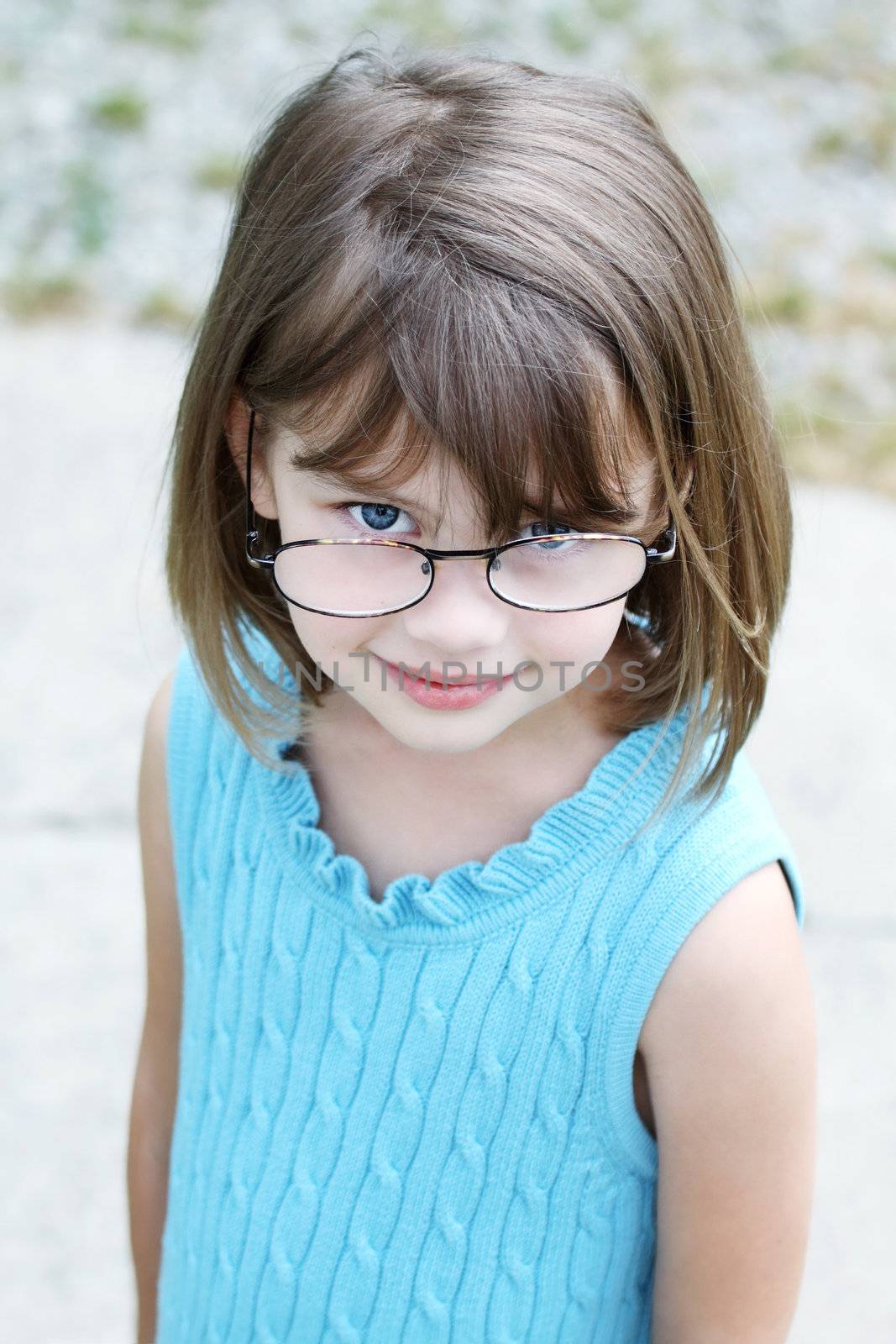 Little girl outdoors wearing glasses and looking up into the camera.

