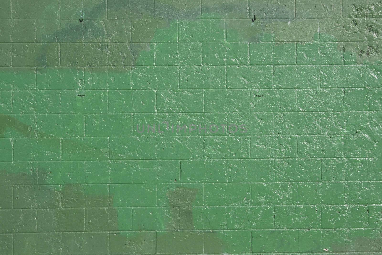 green brick wall that has been covered up with off shades of green to cover grafitti.