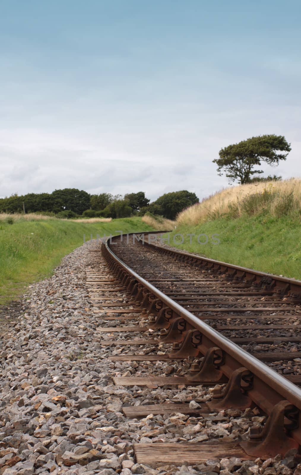 A low angled image of steel railway tracks and wooden sleepers. Track curves at the mid horizon point around a corner. Location is on the Swanage Steam Railway Network in Dorset, UK.