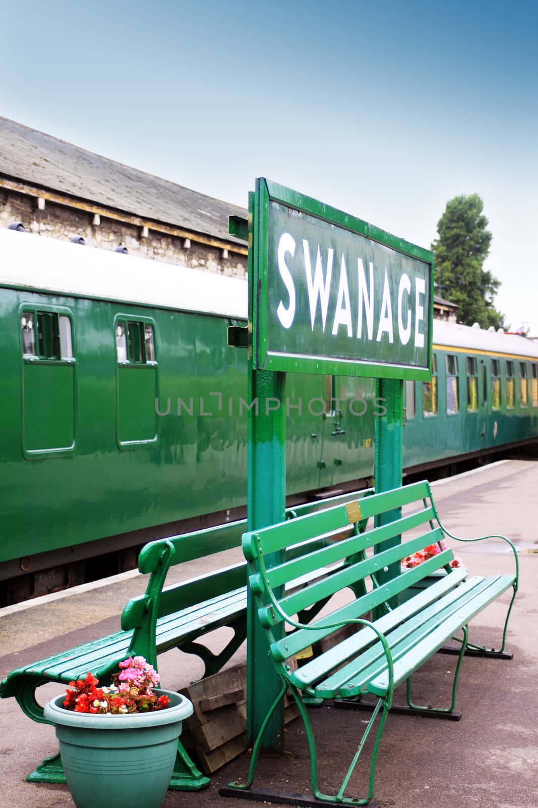 The train platform at Swanage Railway, Dorset UK. Image show the platform signage, platform benches and passenger train carriages.