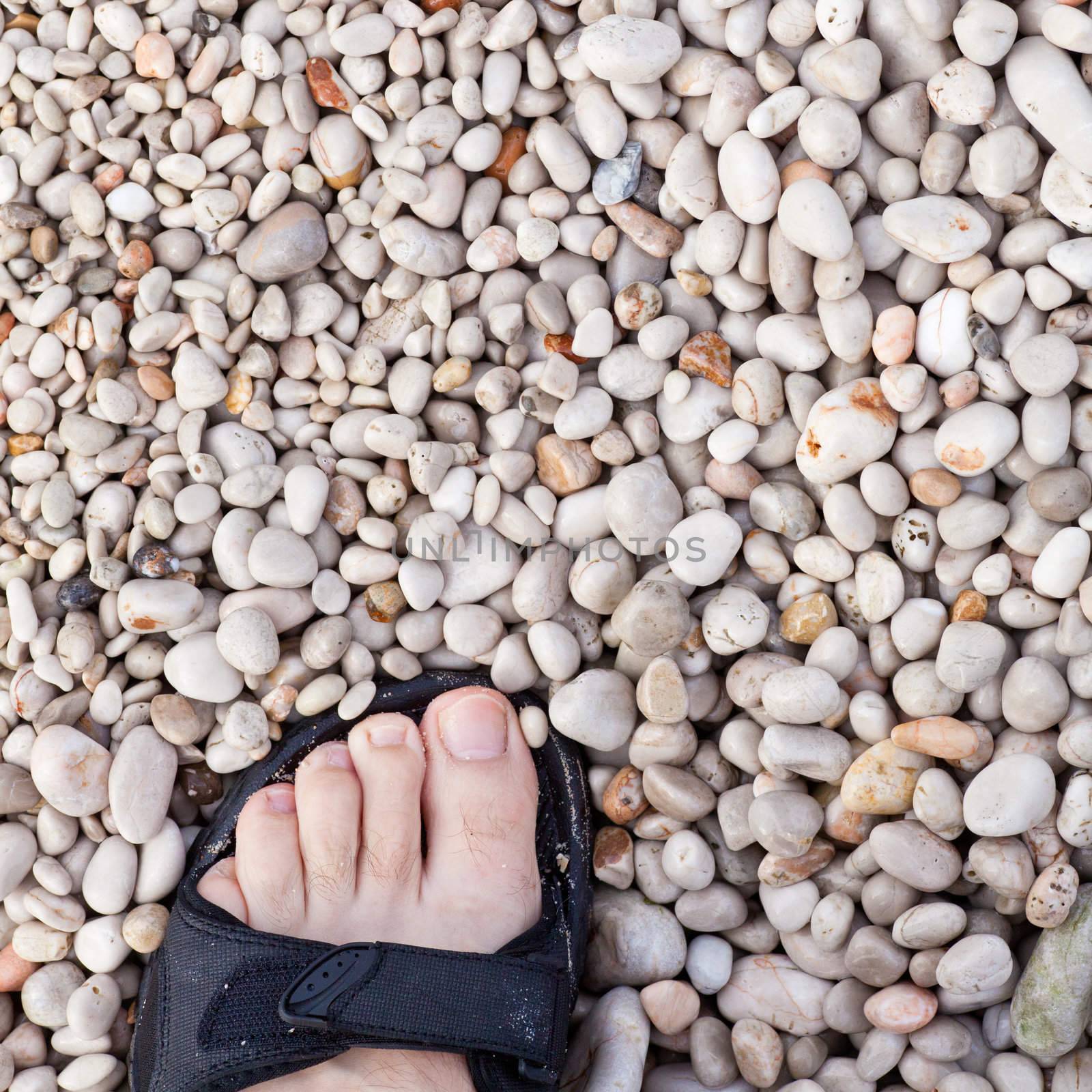 Naked toes in sandal on naturally rounded gravel at sea shore.