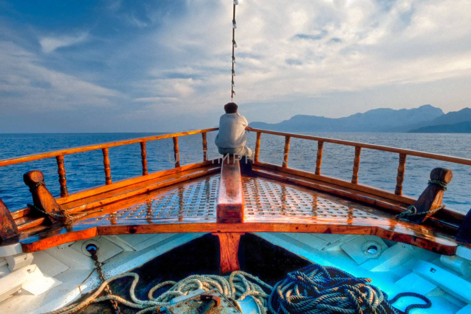 Man day-dreaming at the bow of traditional Greek vessel cruising the aegean sea.