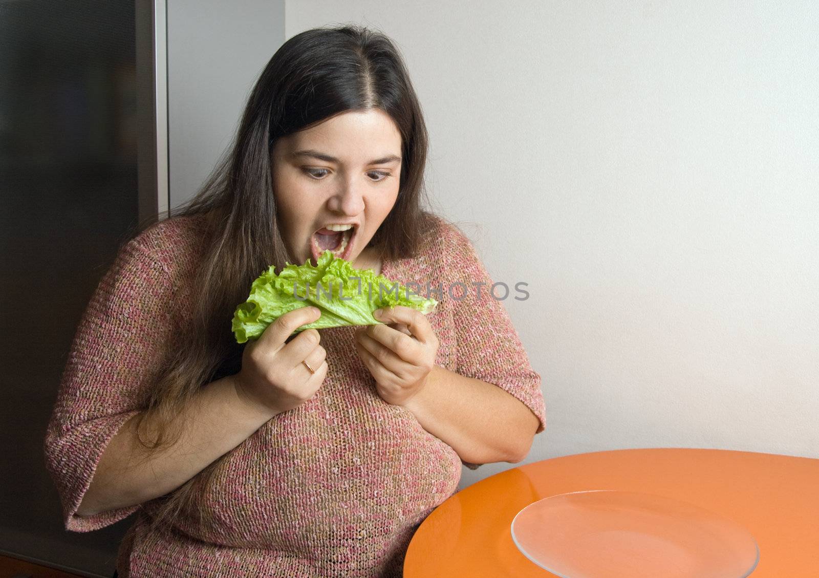 Stout woman trying to eat a leaf of lettuce