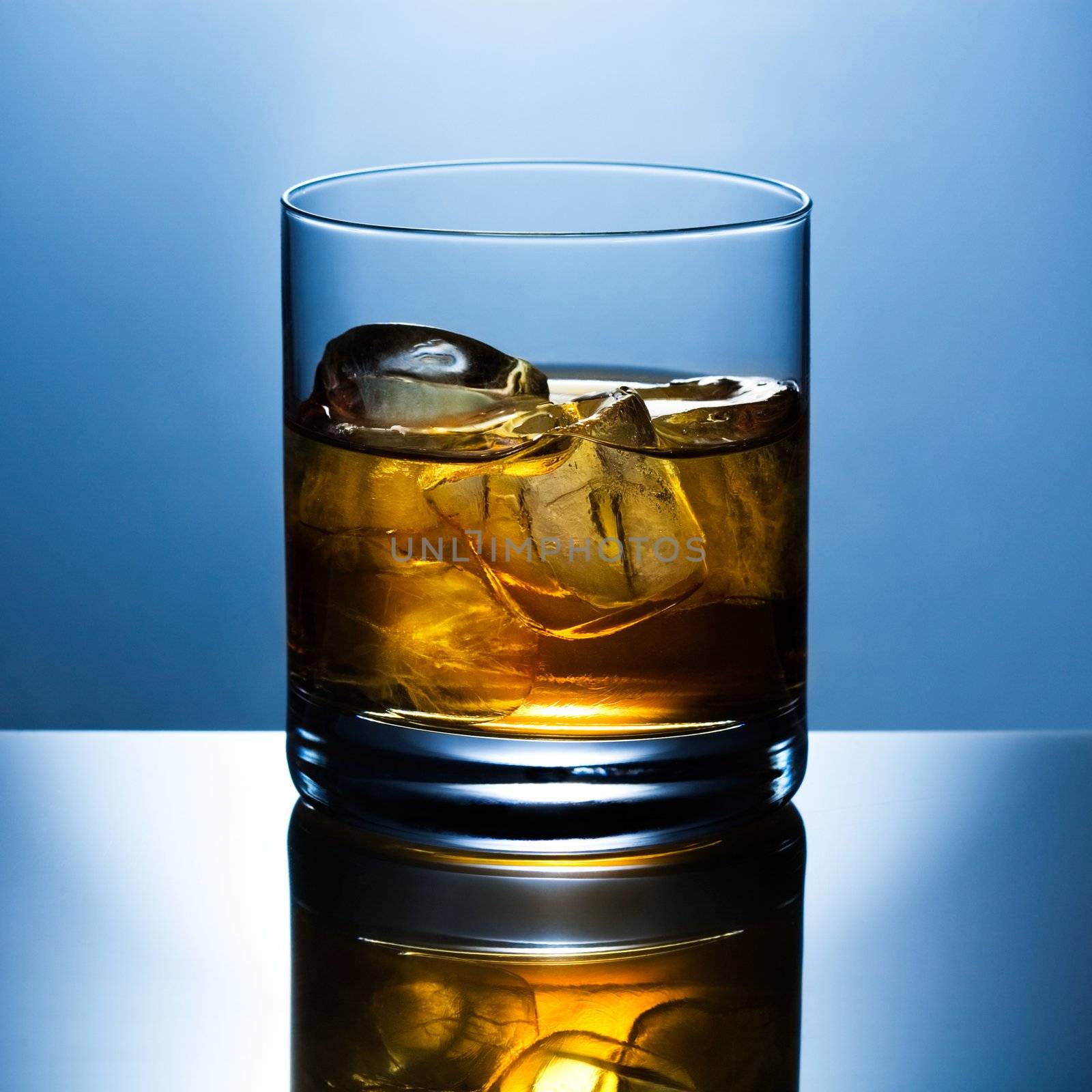 Beautifully shined glass from whisky with ice is reflected in a glass table
