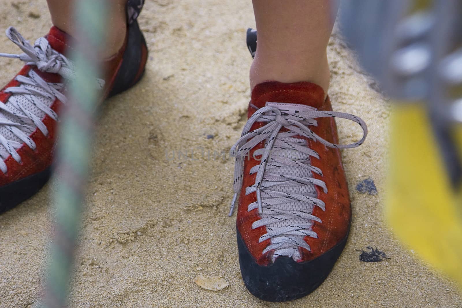 A close-up of a woman rock climber's shoes, with rope and gear out of focus in the foreground. 