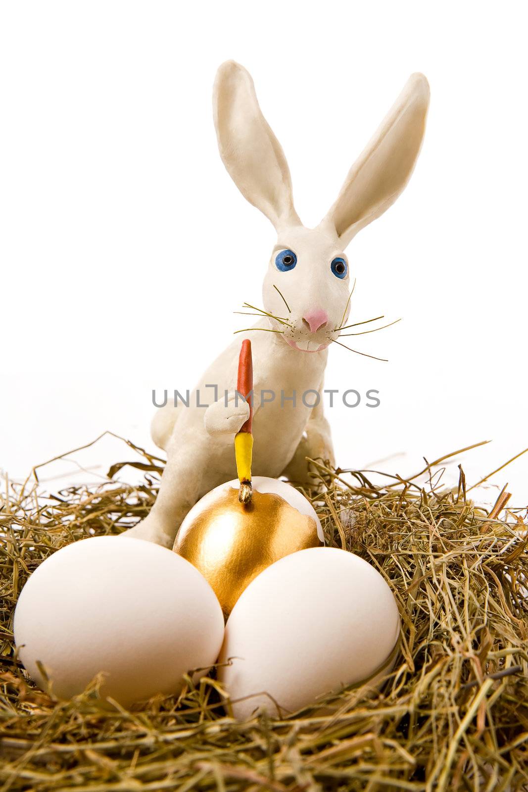 The white rabbit paints egg in gold colour in a nest
