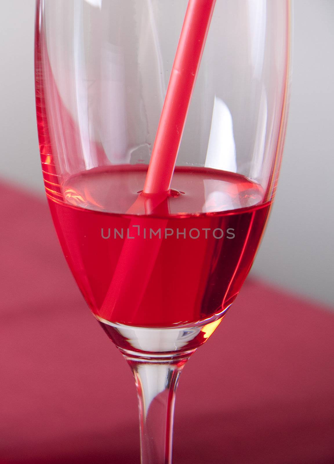 Red cocktail in a glass with a straw on a red table