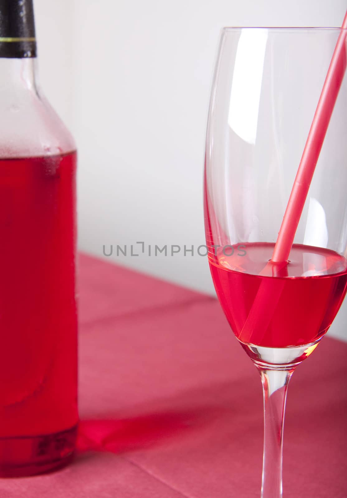 Red cocktail in a glass with a straw and a bottle on a red table