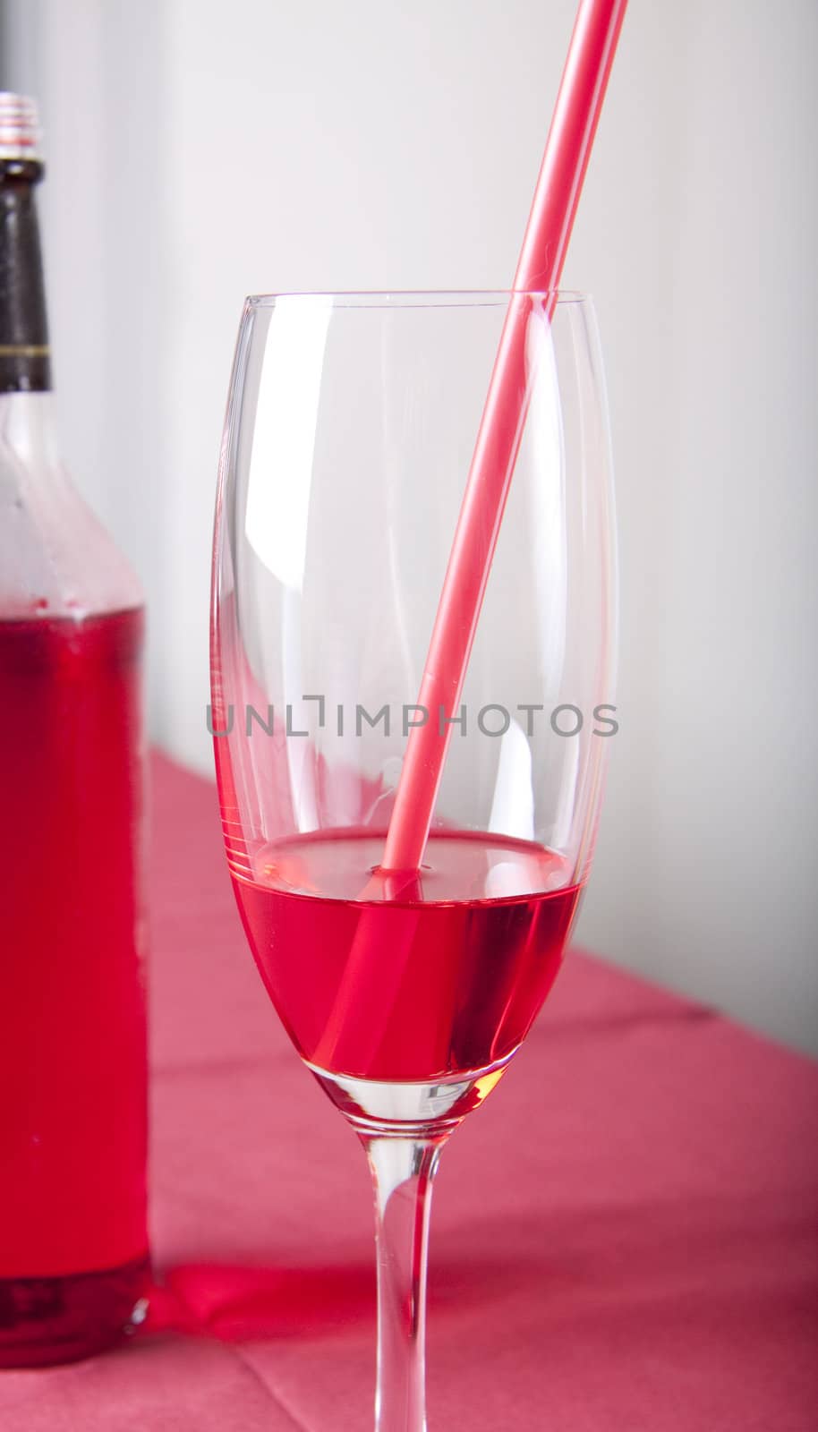 Red cocktail in a glass with a straw and a bottle