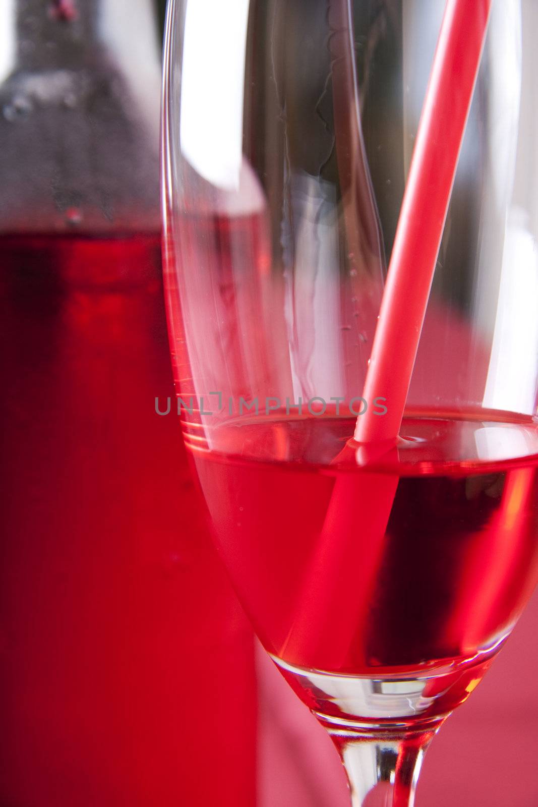 Red cocktail in a glass with a straw and a bottle in the background