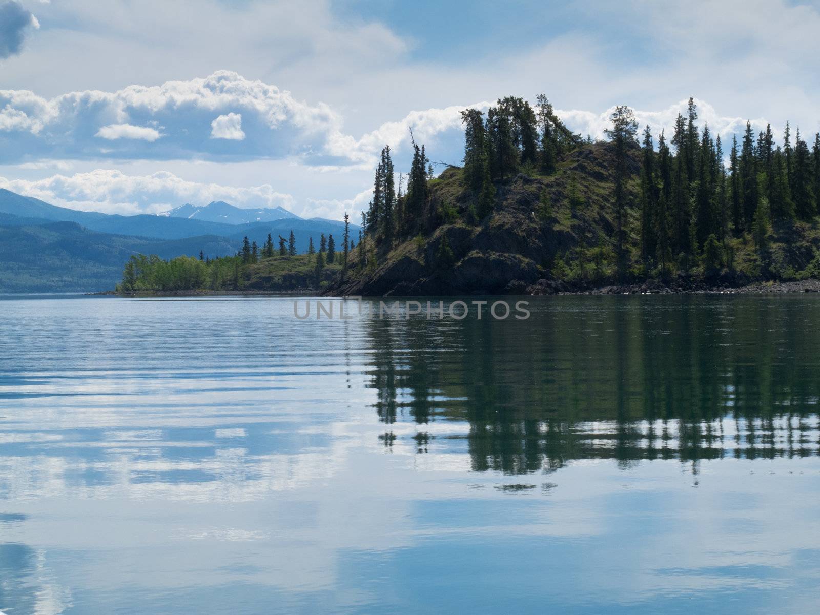 Green forested hills at Lake Laberge, Yukon Territory, Canada are mirrored on water surface on beautiful summer day.