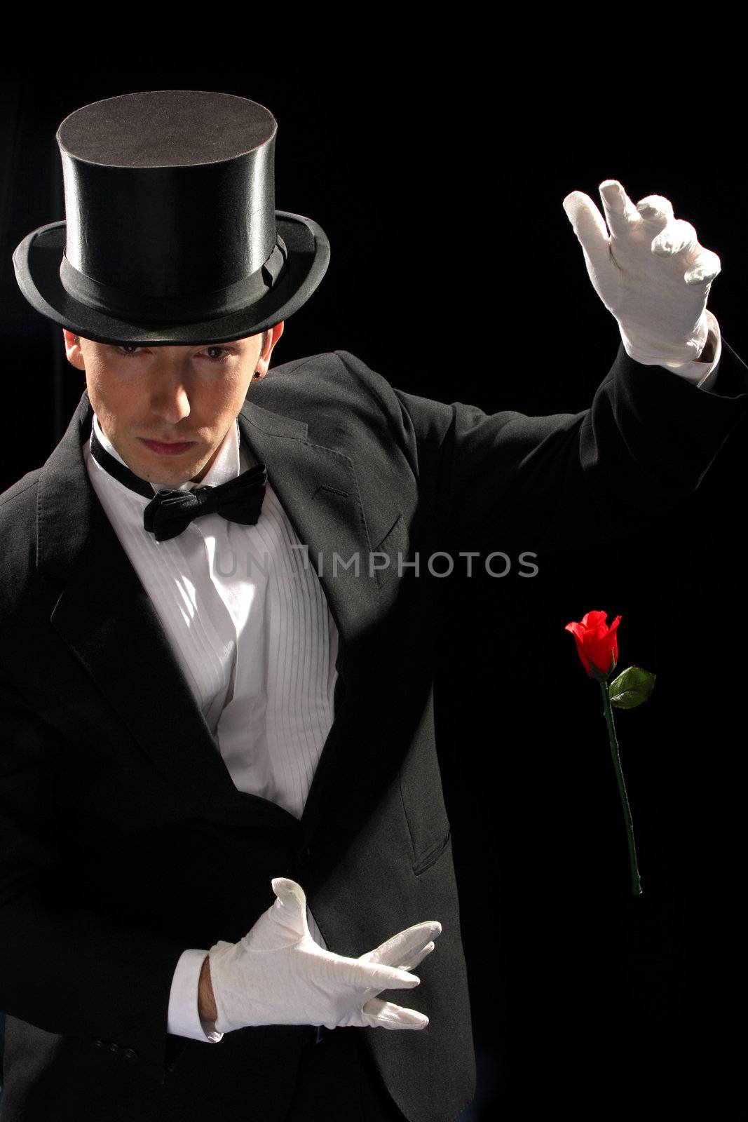 young magician performing red rose on black background