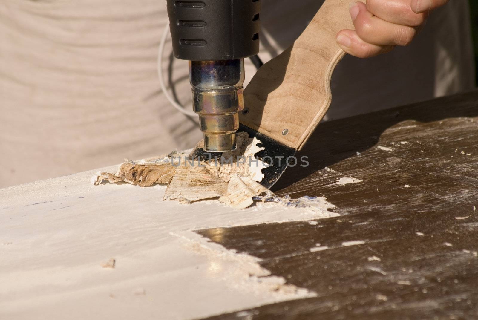 portrait of renovation; removing old paint using scraper and heat gun