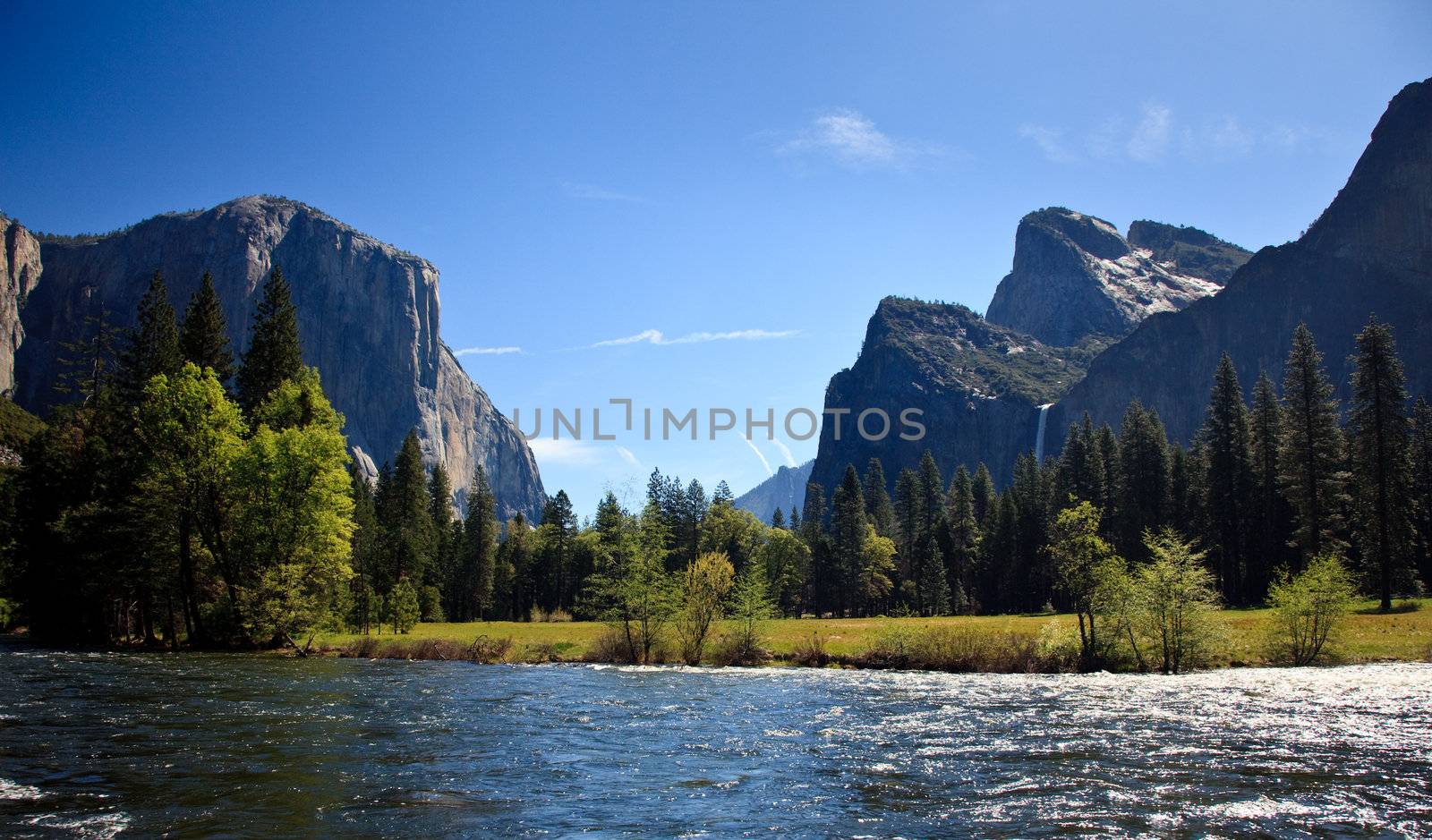 View into Yosemite valley over a shining Merced river showing entrance waterfalls