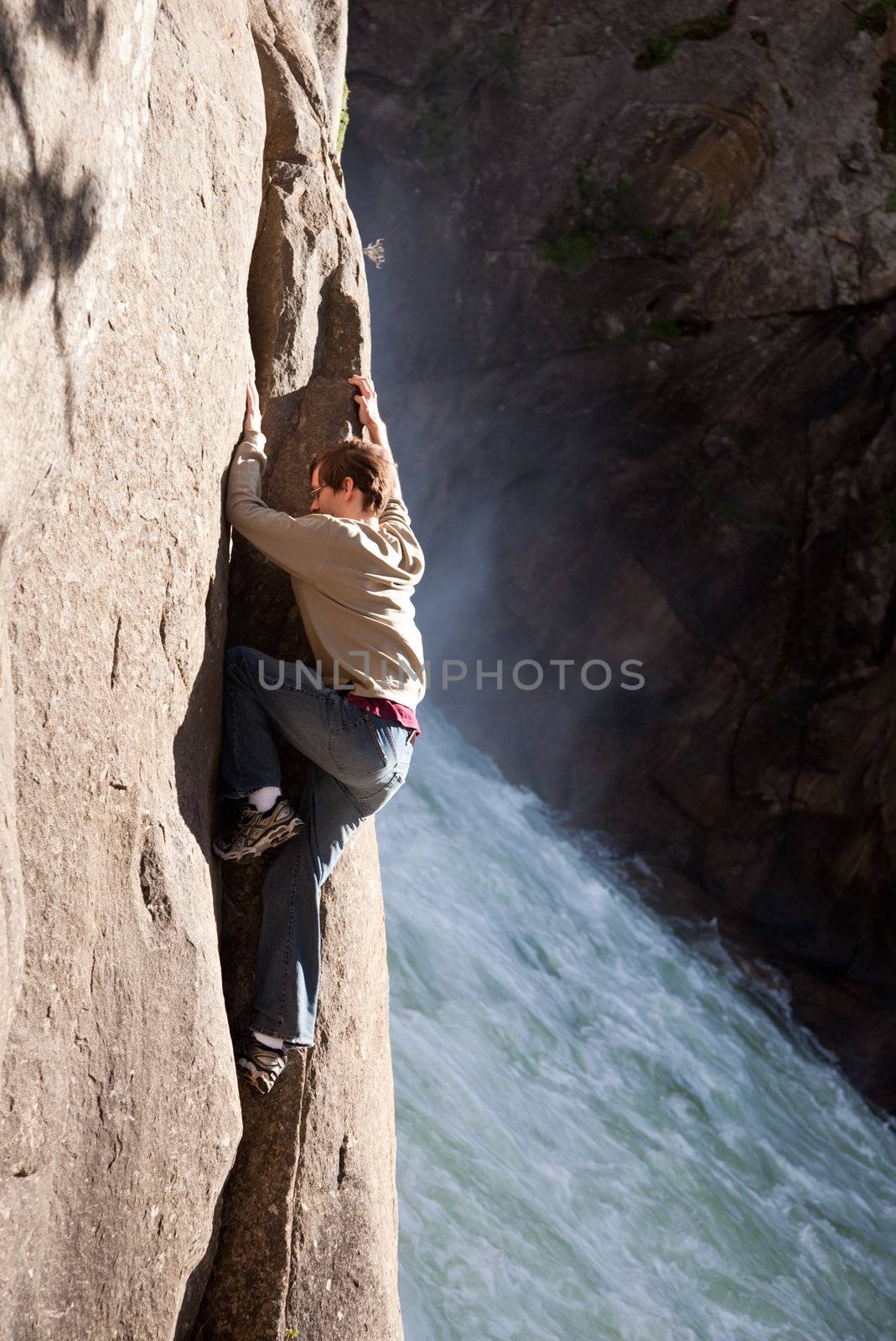 Close up of young male hiker climbing rocks besides a waterfall