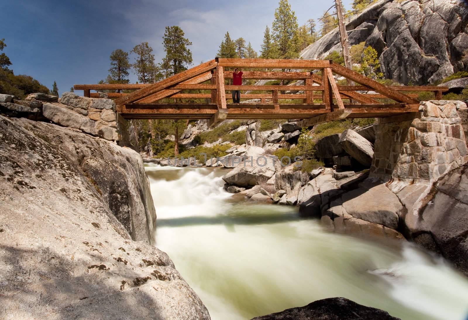 Slow motion photo of Yosemite Falls river with male hiker on the bridge