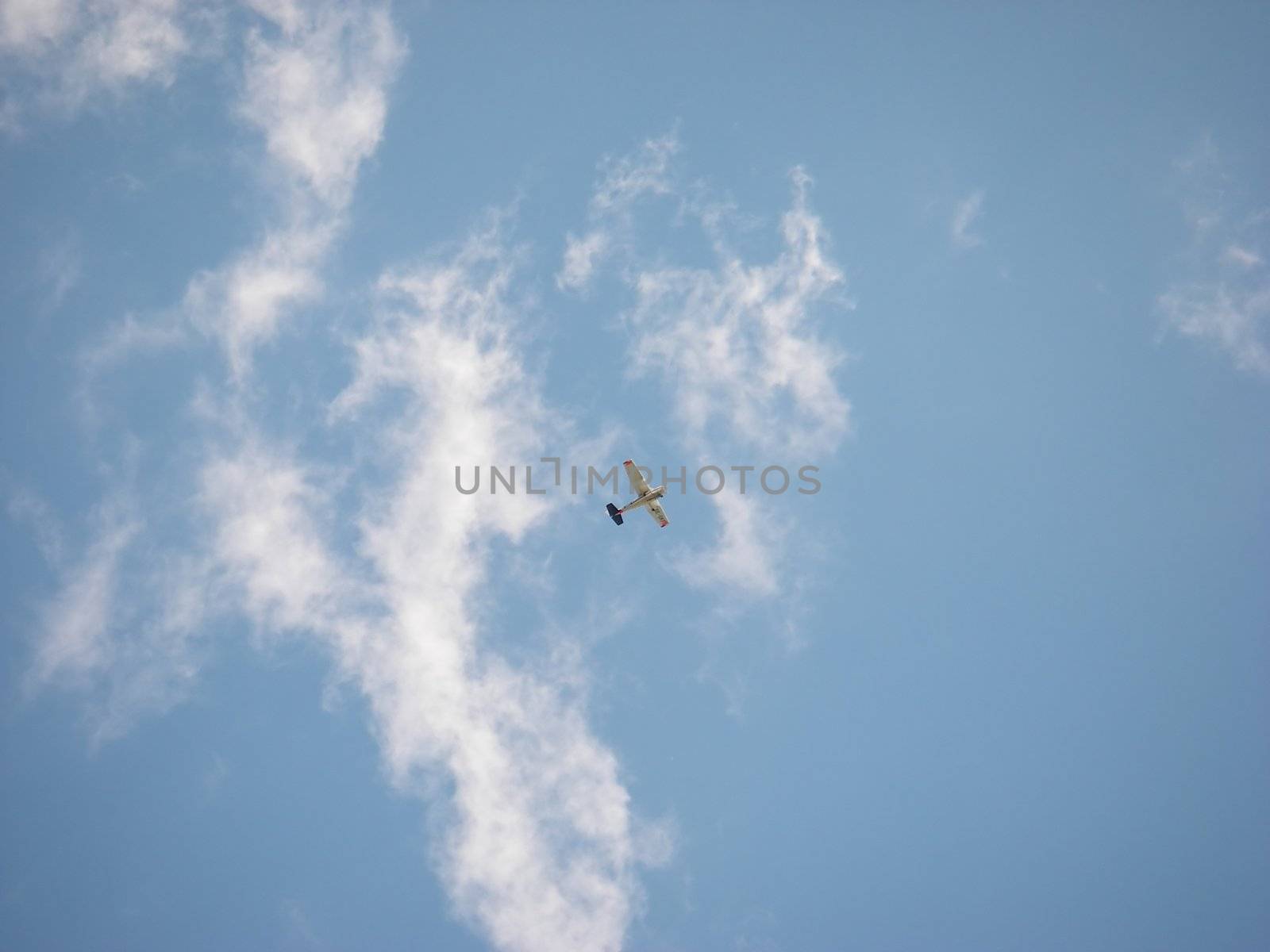 portrait of a small airplane flying in blue cloudy sky
