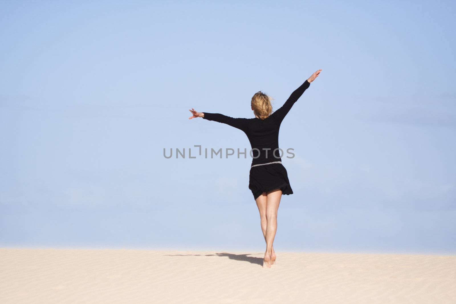 Beautifull girl standing on the sand dune and looking in the distance.