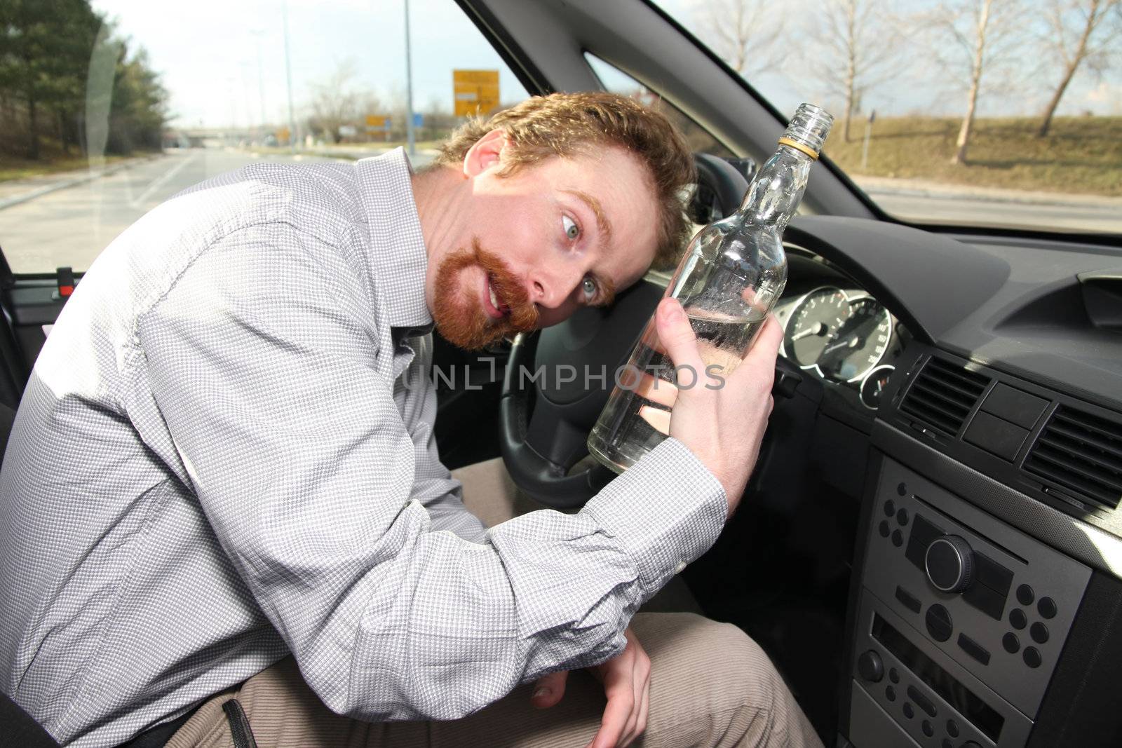 Drunk man sitting in drivers with a bottle alcohol