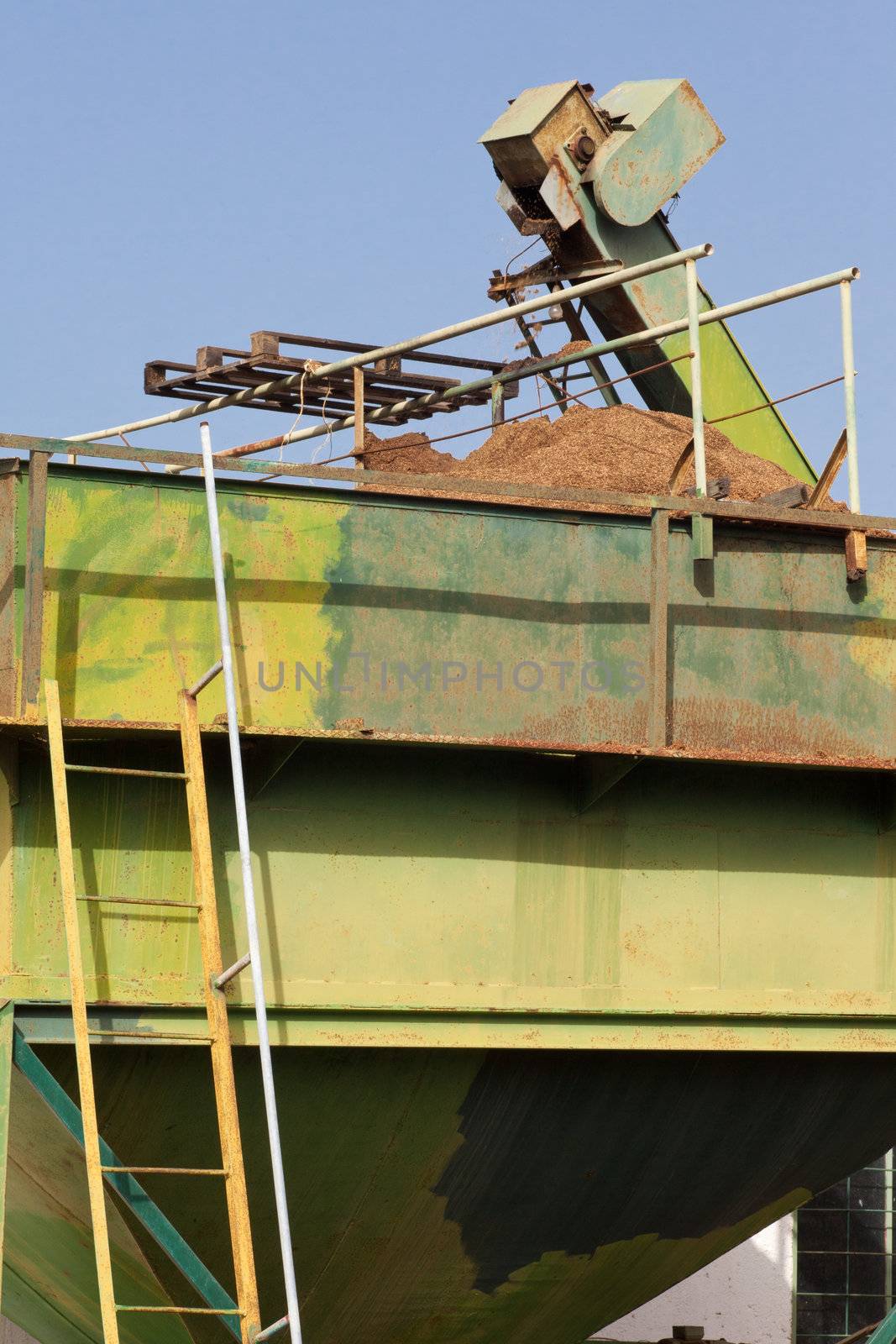 Exhausted olive pulp (orujo) from busy olive oil mill factory being conveyed into huge metal silo container for later composting.