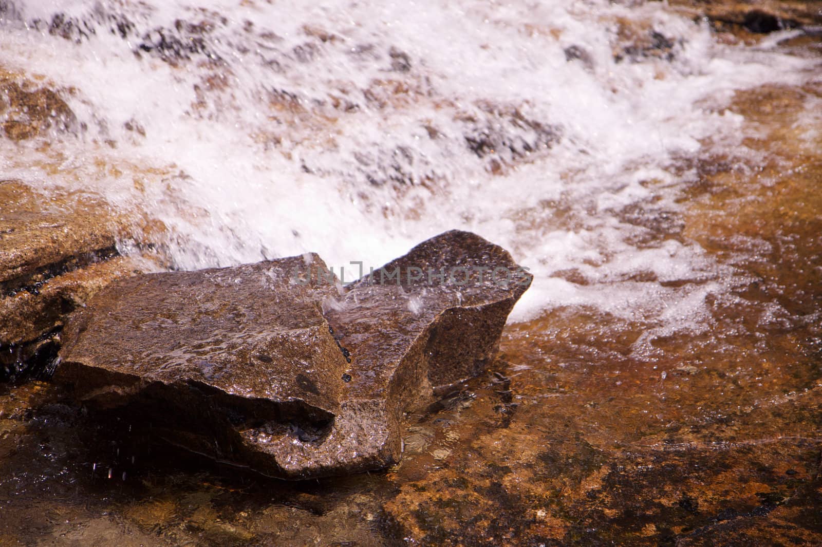 Small single waterfall cascading down mountain boulders with focus on rock