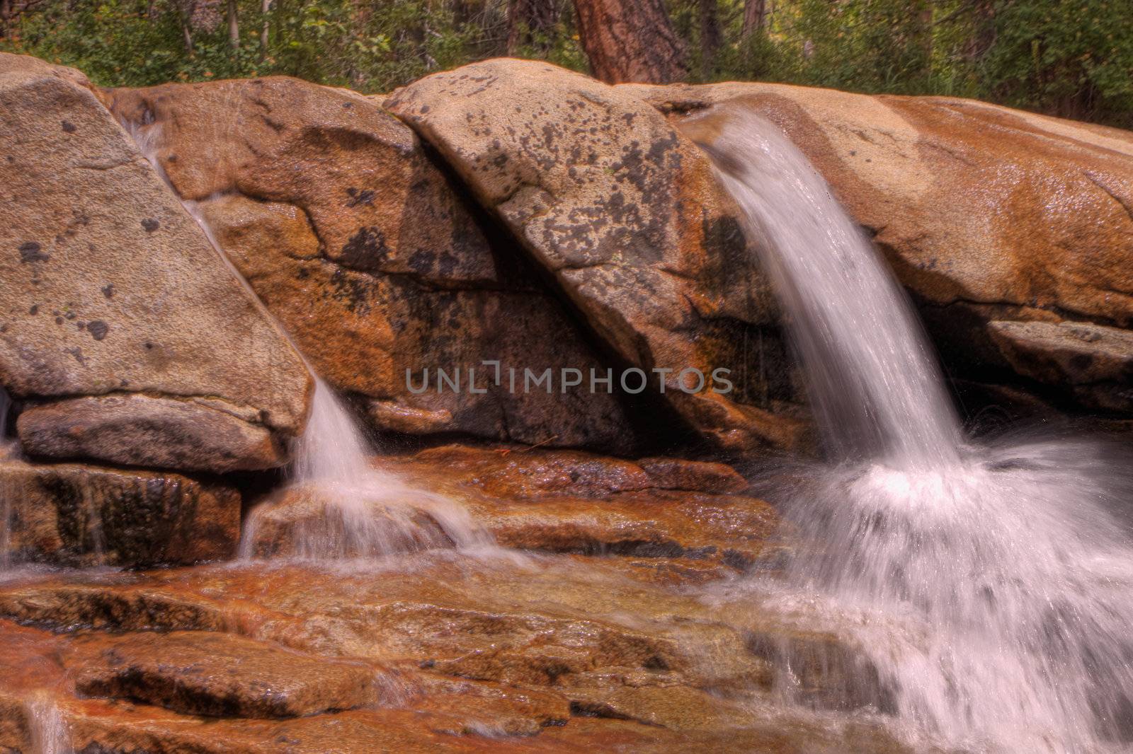 Small  waterfalls cascading down mountain boulders into shallow water in HDR high dynamic range