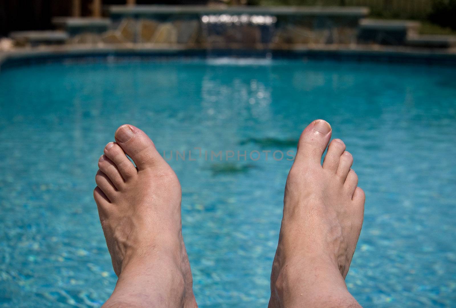 Middle aged male feet overhanging a blue swimming pool