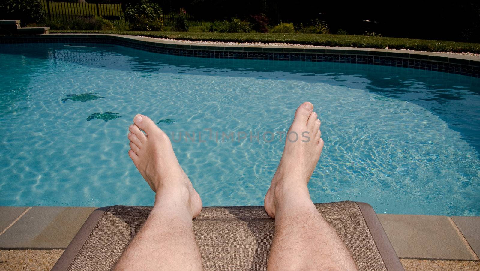 Middle-aged man's feet overhanging blue swimming pool