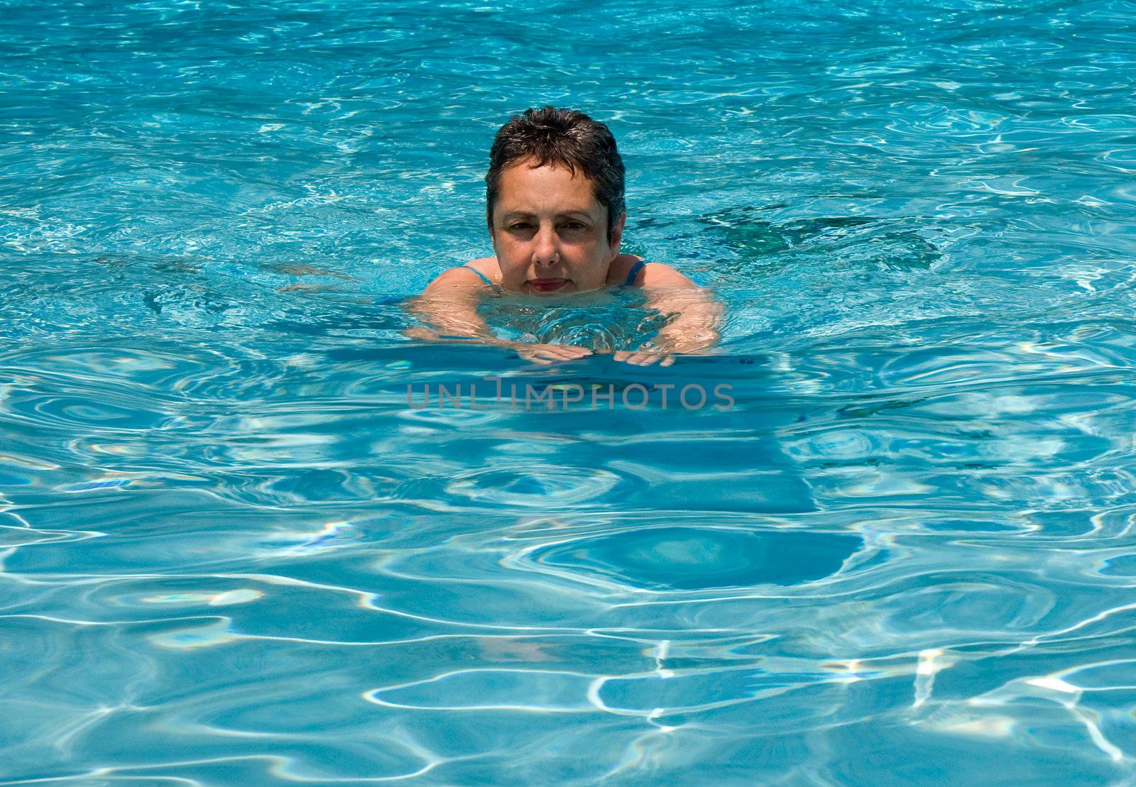 Middle aged woman swimming in blue open water towards camera