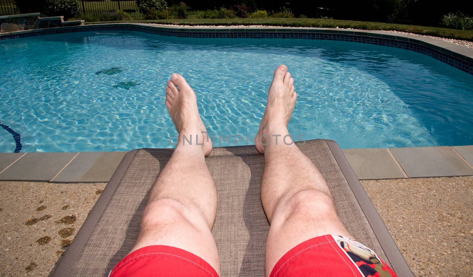 Middle aged man's legs overhanging blue swimming pool