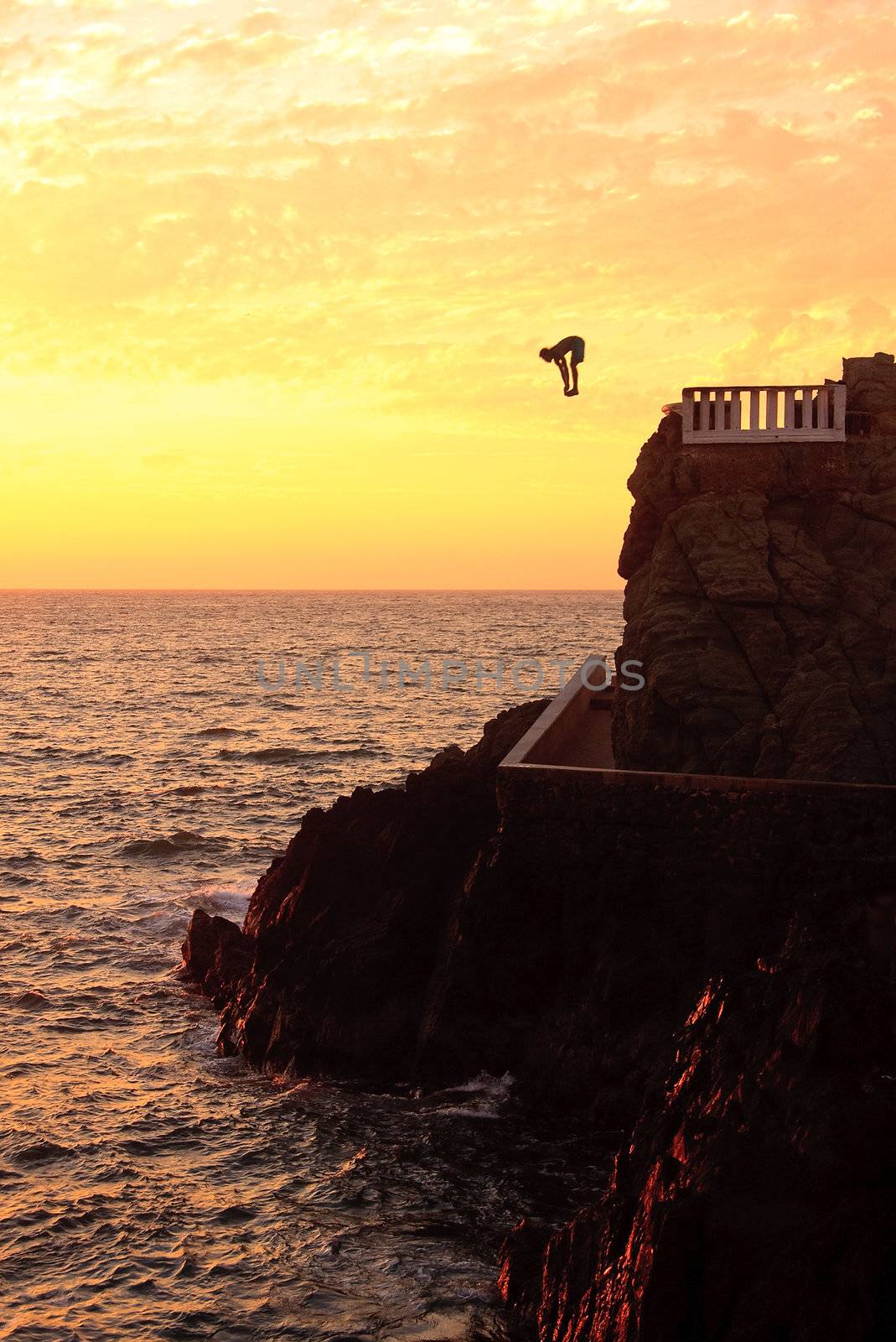 Young diver diving into the sea off the sea cliffs at Mazatlan as the sun sets