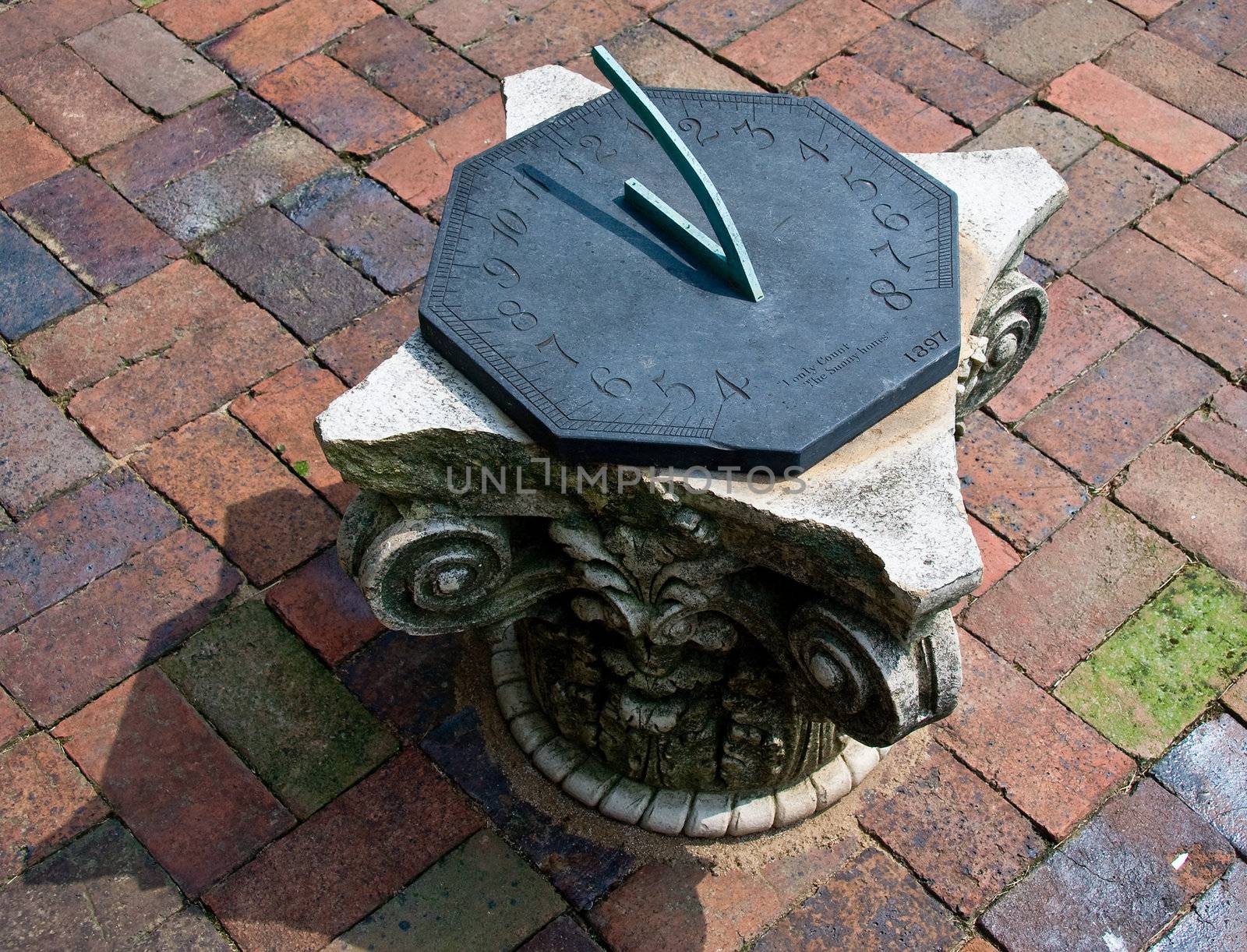 Close-up of sun dial on brick patio on carved stone plinth