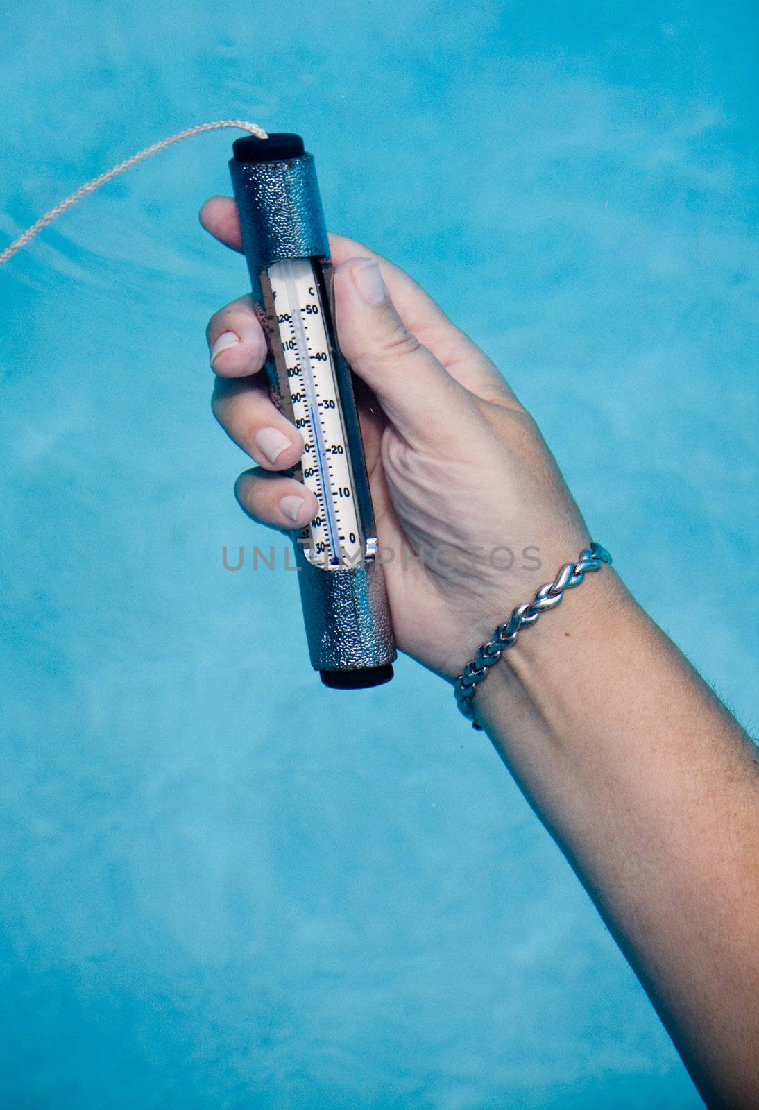 Female hand holding pool thermometer under water