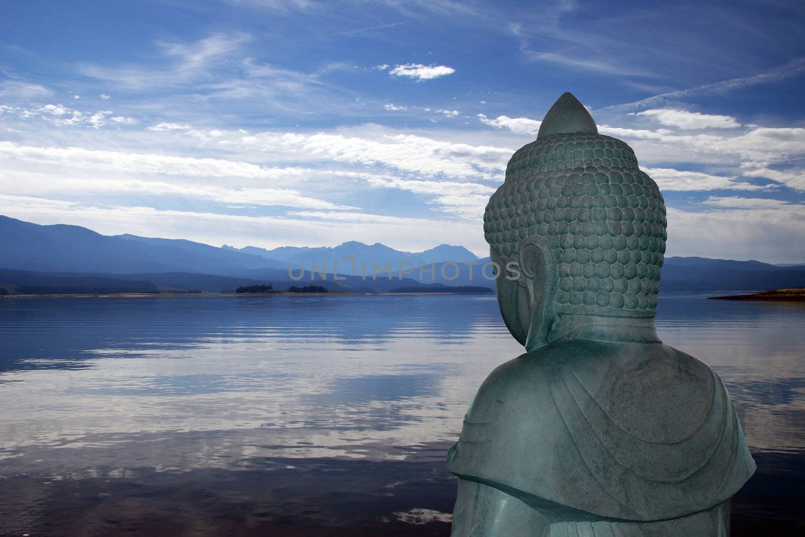 Backview of Buddha statue overlooking a peaceful mountain lake