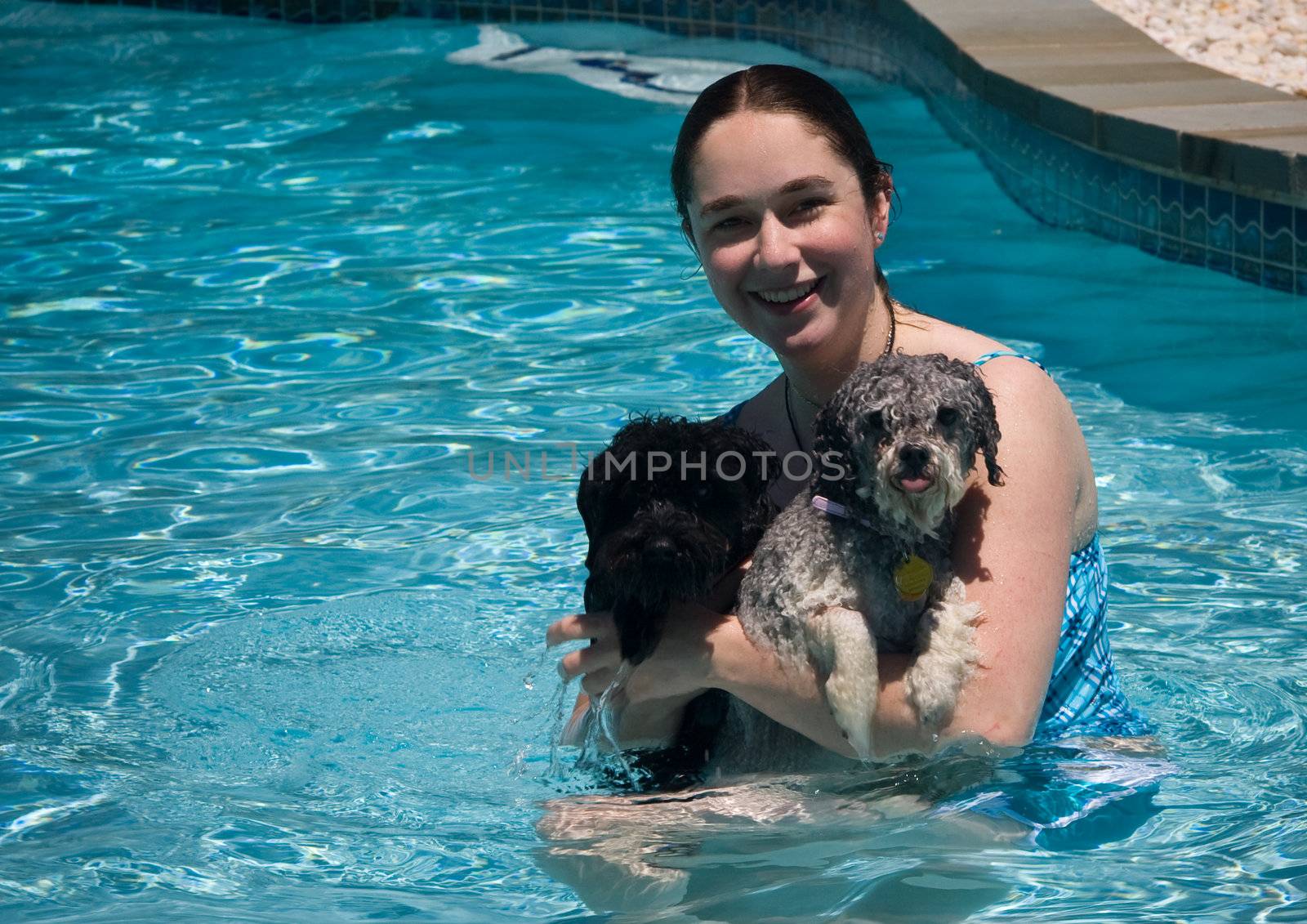 Woman and two small dogs in her arms in a blue swimming pool