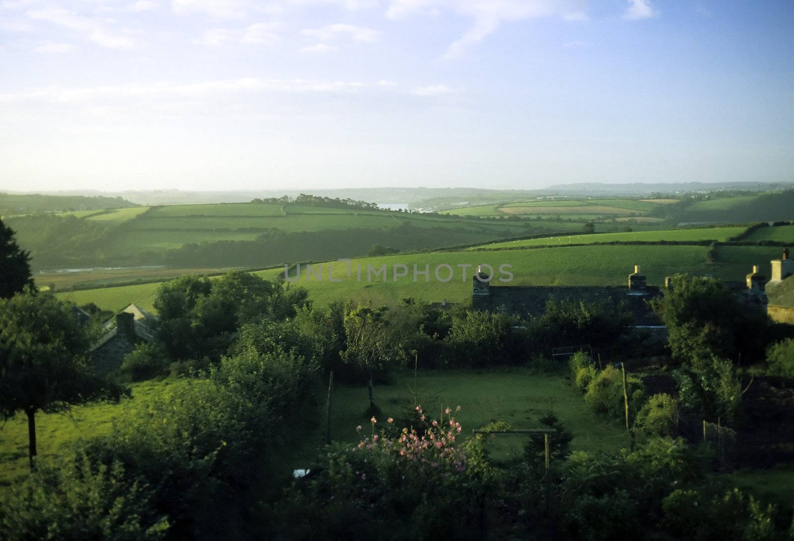 View over lush green  english countryside in summer with a cottage garden in the foreground