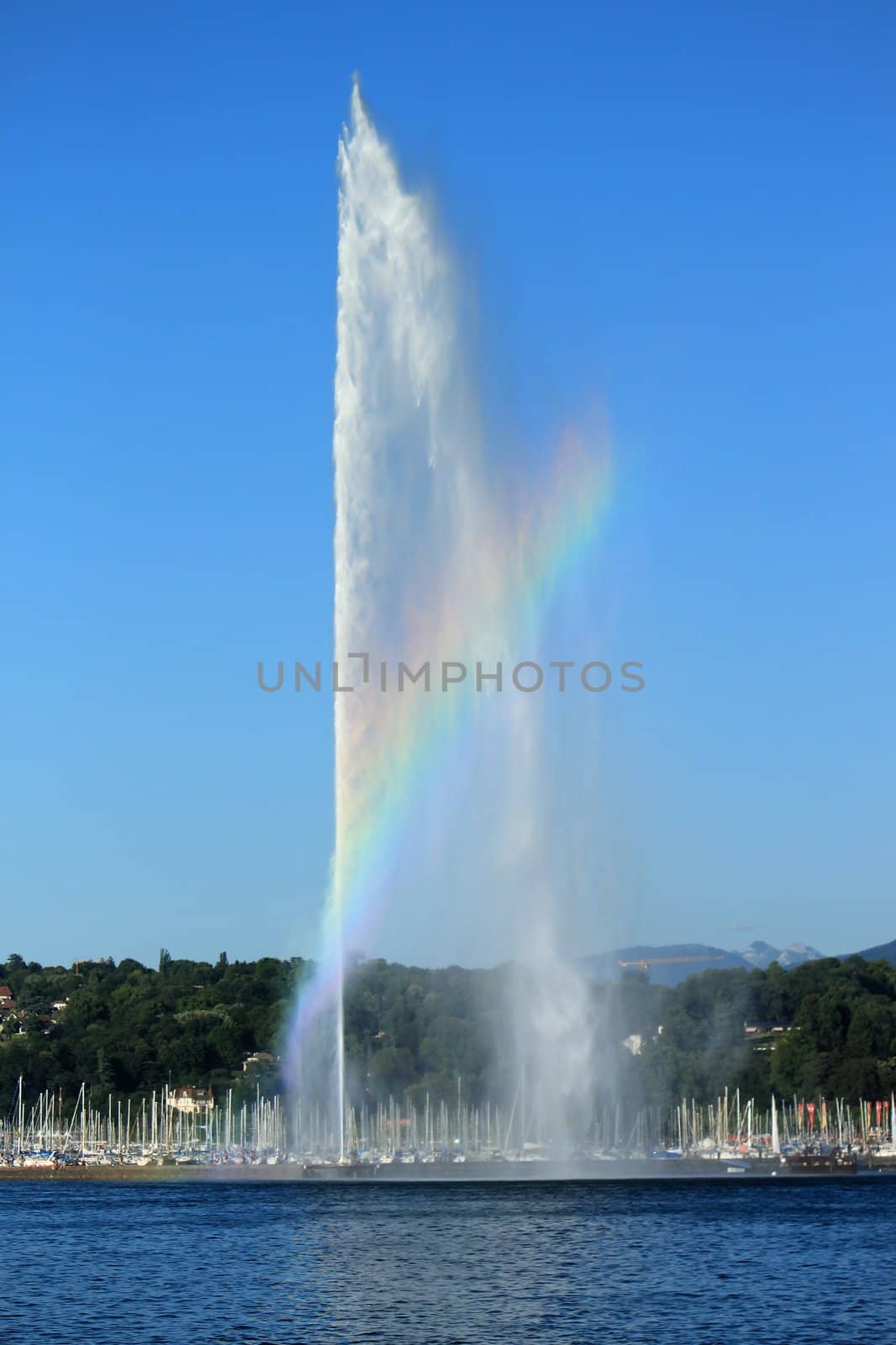 A beautiful rainbow colors the mist on the 140 m water fountain on Geneva Lake, Geneva, Switzerland. It is the symbol of this swiss city and is called the Jet D'eau.