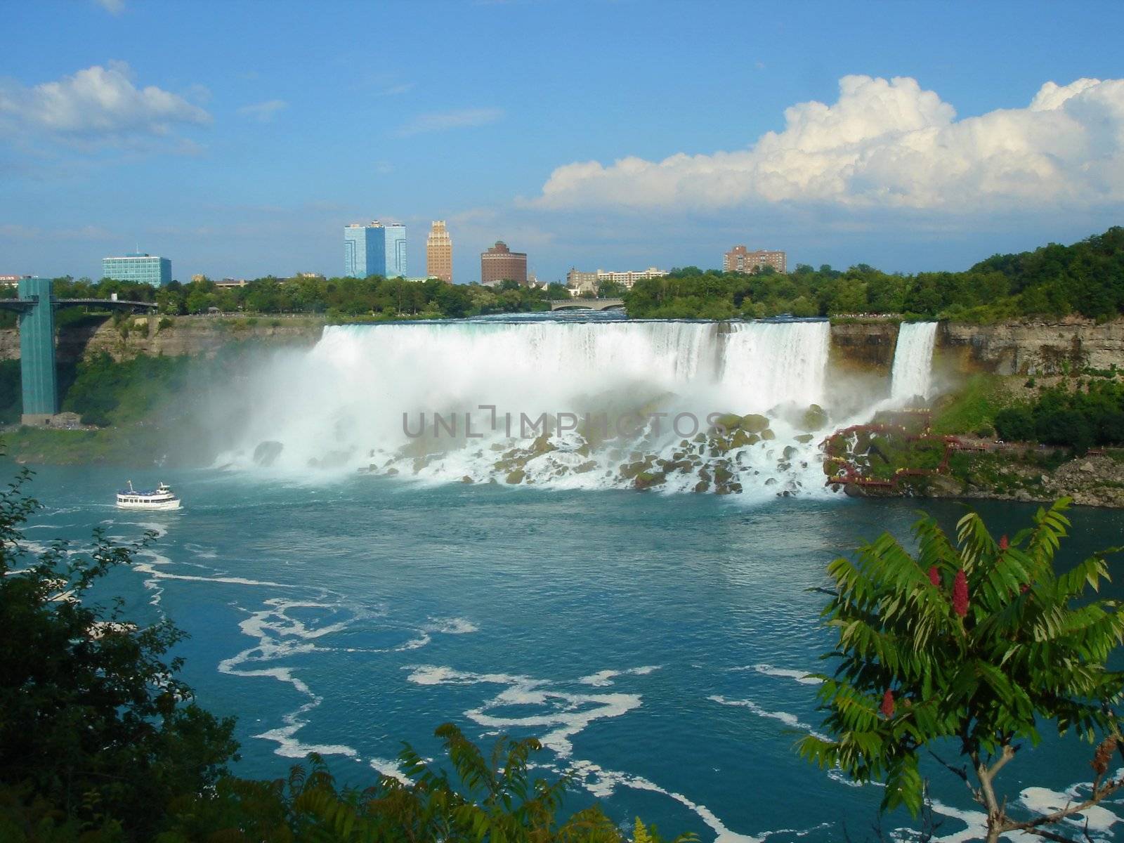 Niagara falls from far with boat and buildings and vegetation