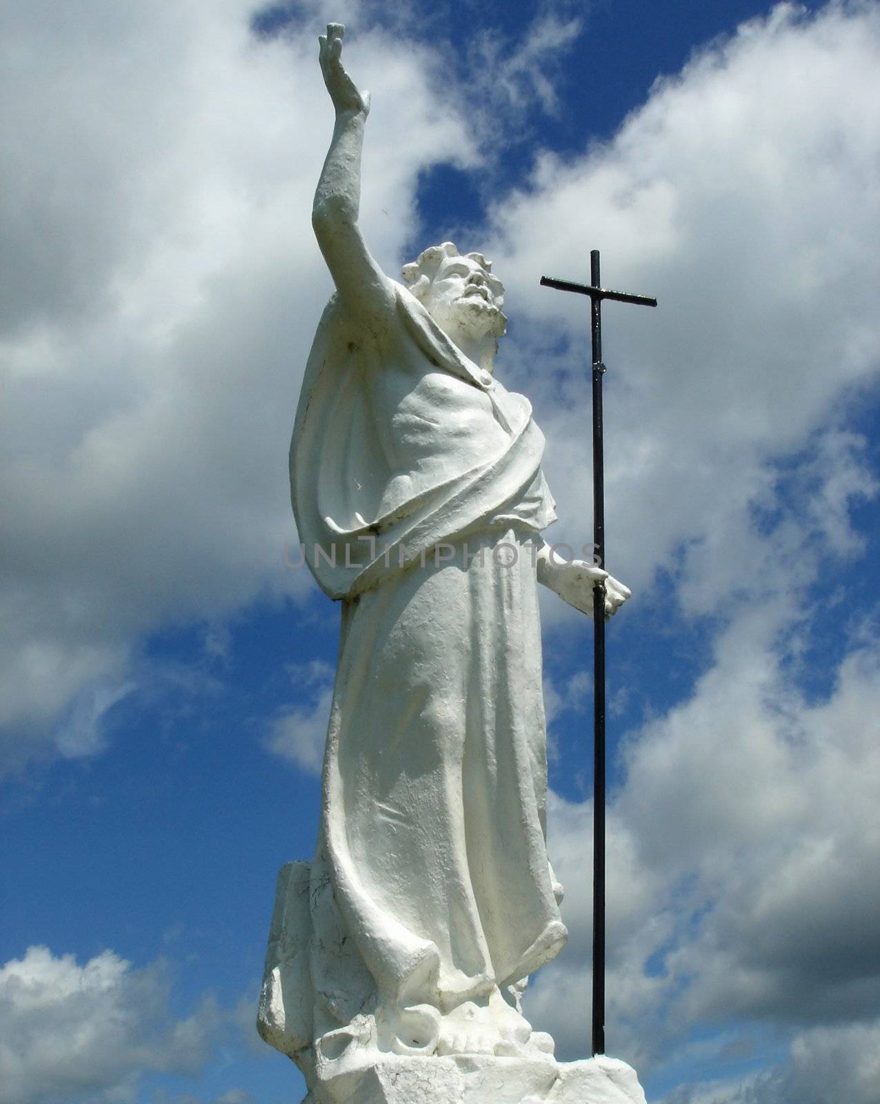 White statue of Jesus-Christ with a cross in one hand and with the other hand up while praying God