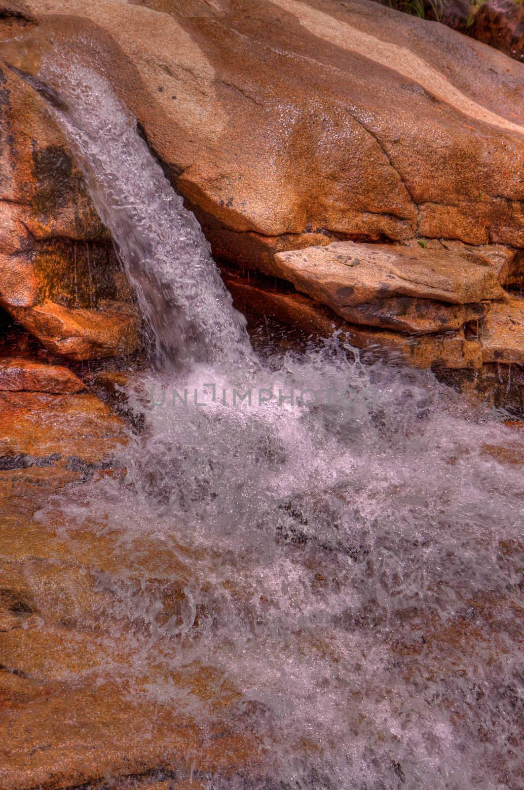 Small single waterfall cascading down mountain boulders into cascading water in HDR high dynamic range