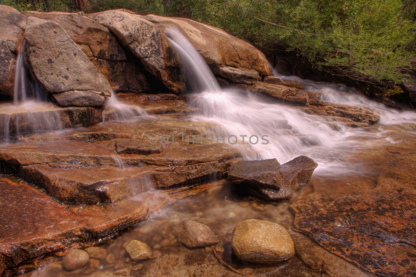 Small single waterfall cascading down mountain boulders into shallow water in HDR high dynamic range
