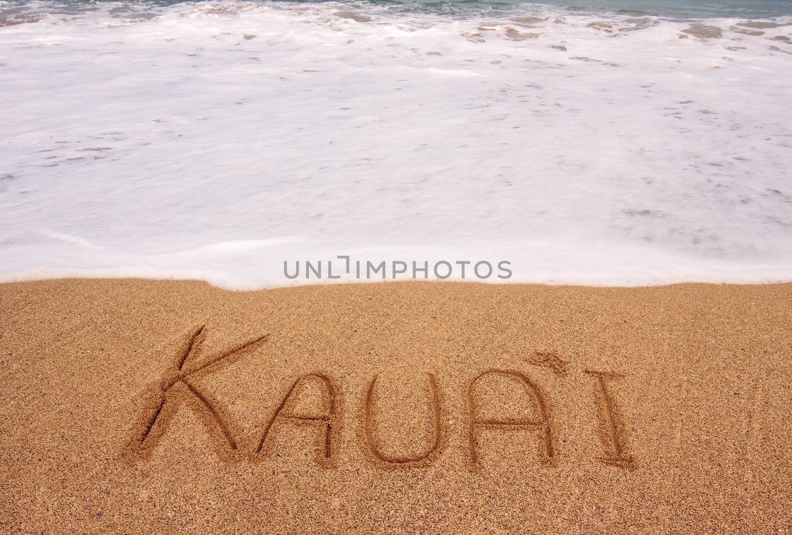 White foam of the tide coming towards the name Kauai scratched in the sand